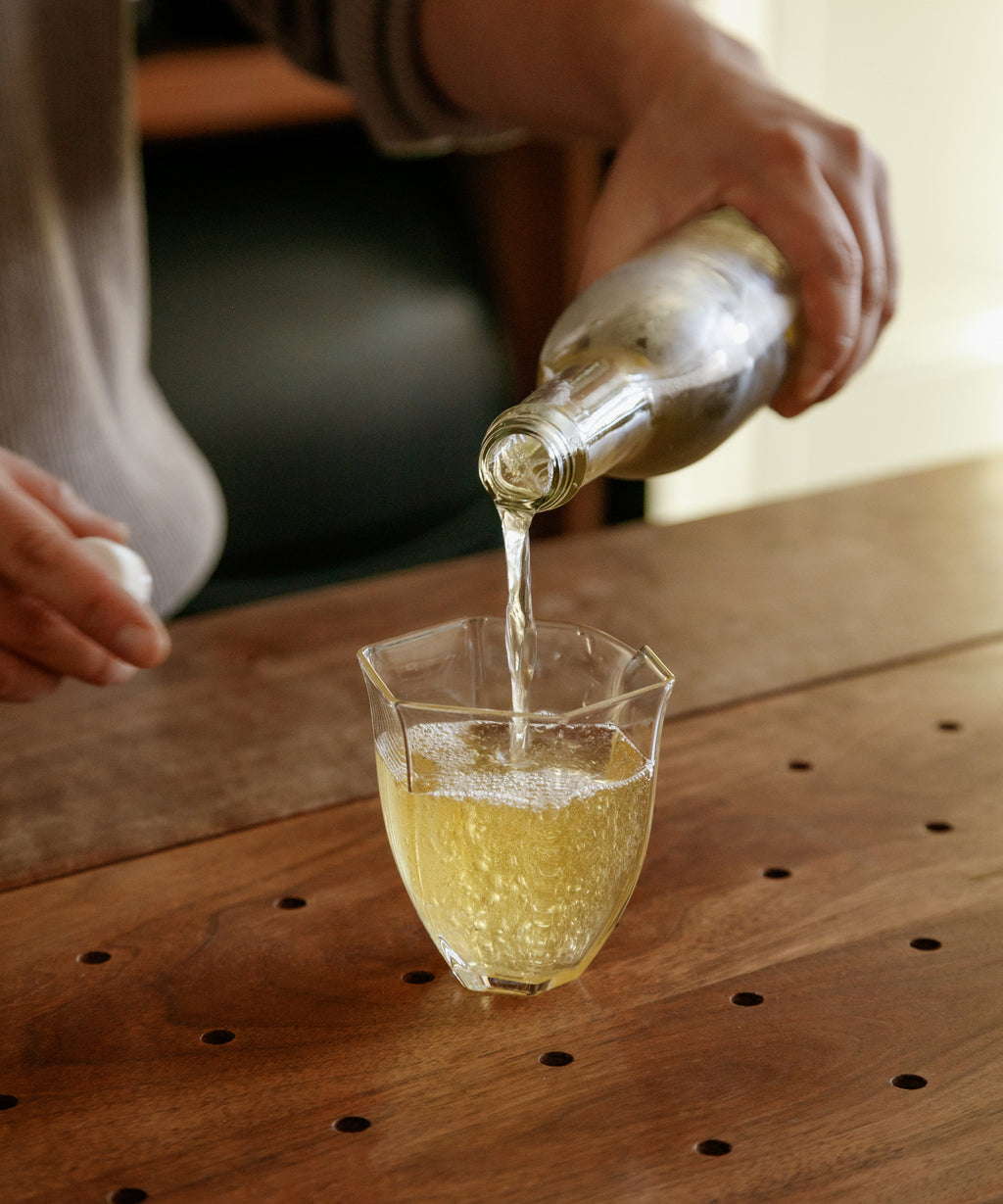 Pouring Noma Koshun sparkling hojicha from bottle into a glass, showing golden effervescent liquor