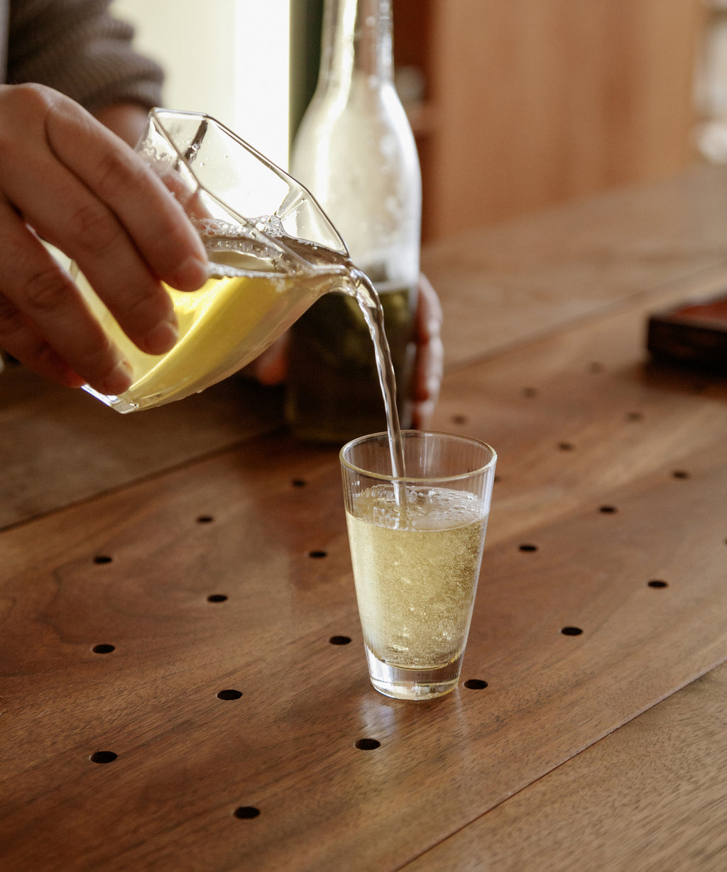Pouring Noma Koshun hojicha from a glass pitcher into a tall glass, sparkling and refreshing