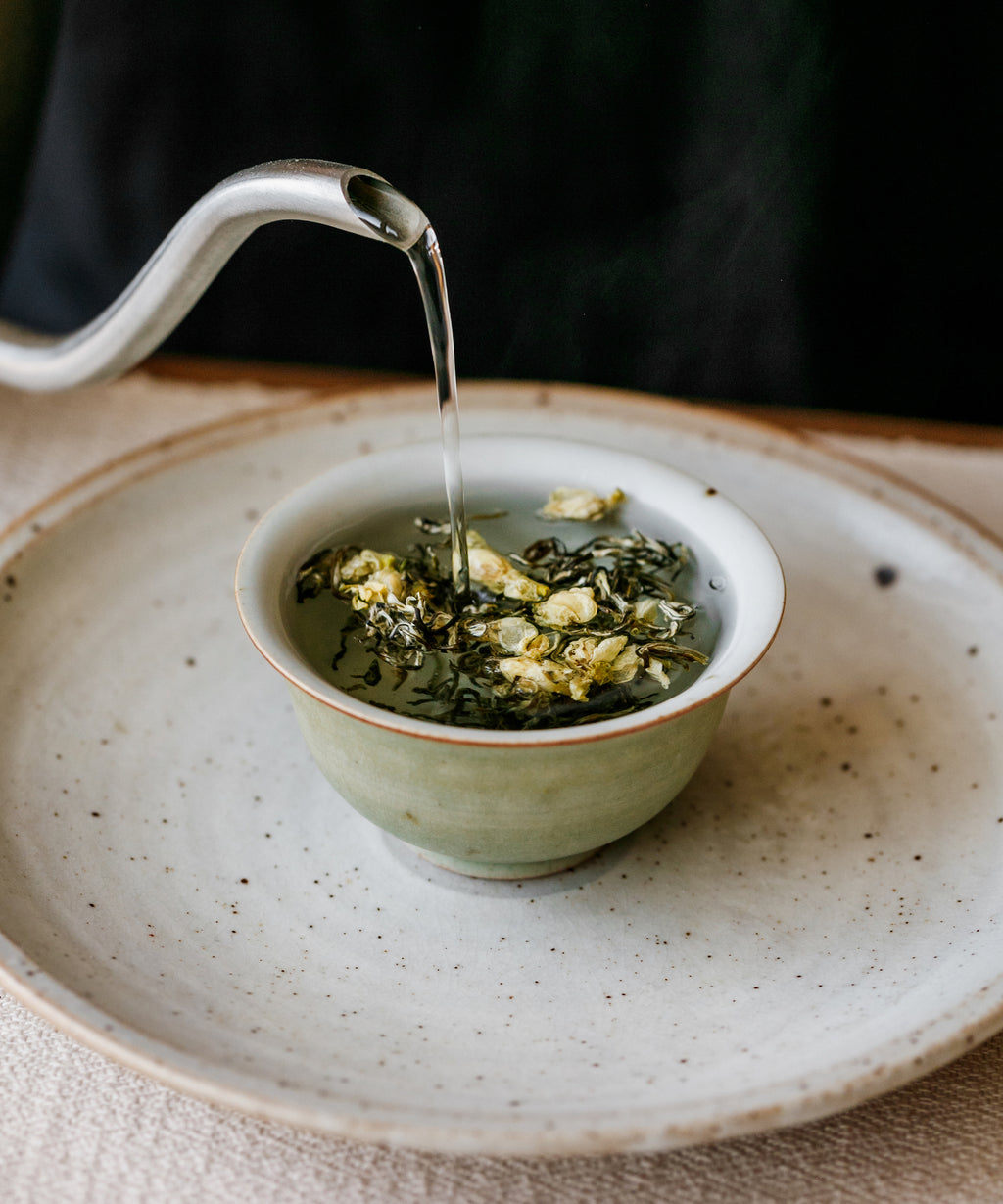 Hot water poured over Jasmine Snow Flake tea in a white preparation bowl