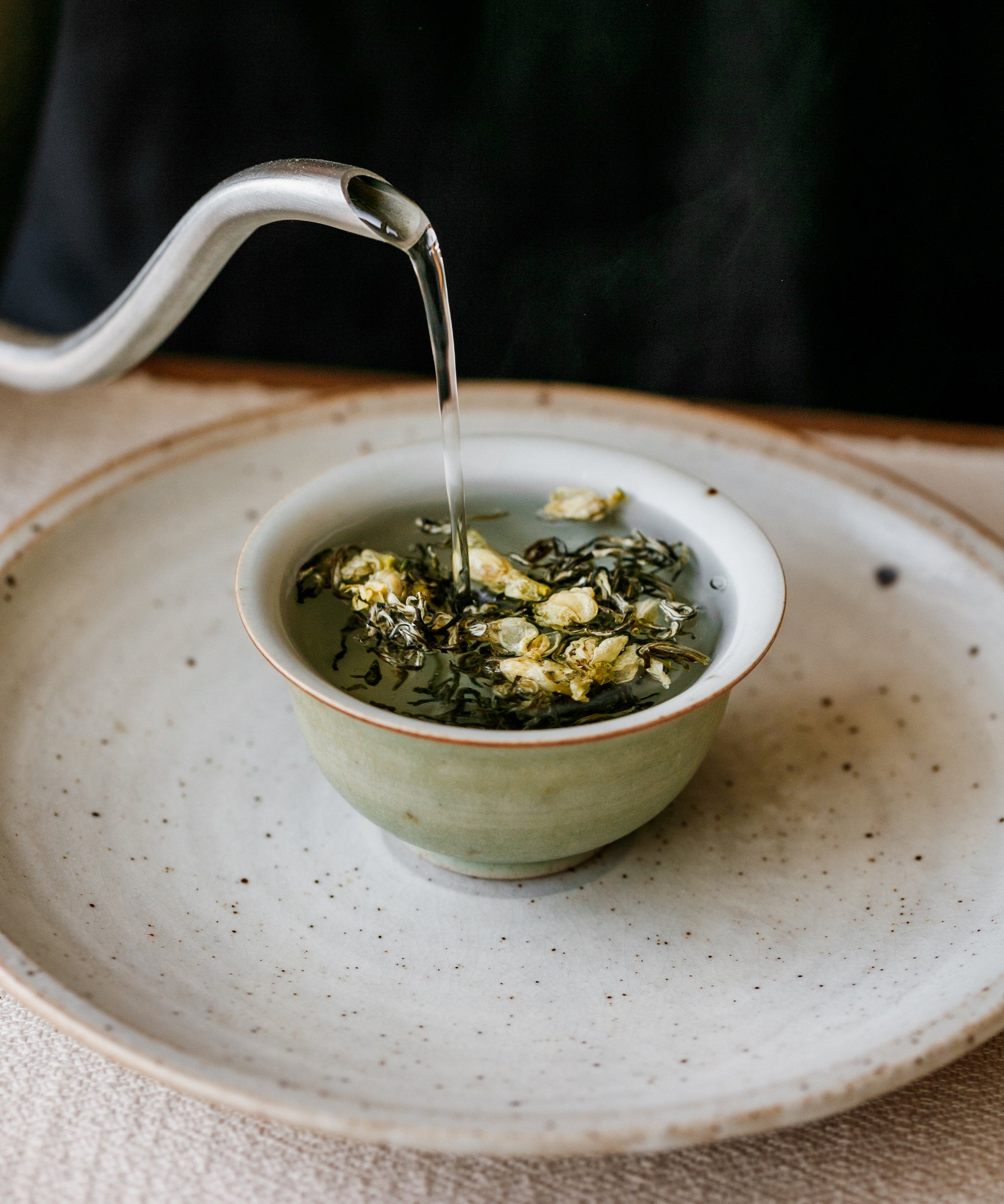 Hot water poured over Jasmine Snow Flake tea in a white preparation bowl