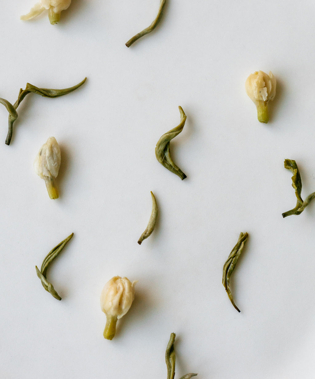 Scattered dried jasmine and tea pieces on white - Jasmine Snow Flake green tea from Emei Mountain, Sichuan