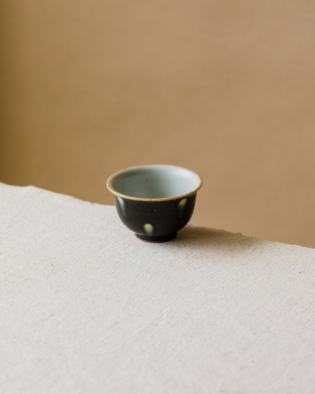 Cup Black Peacock in hand, peacock-iris pattern on matte black, Wang Xinghua gongfu teaware