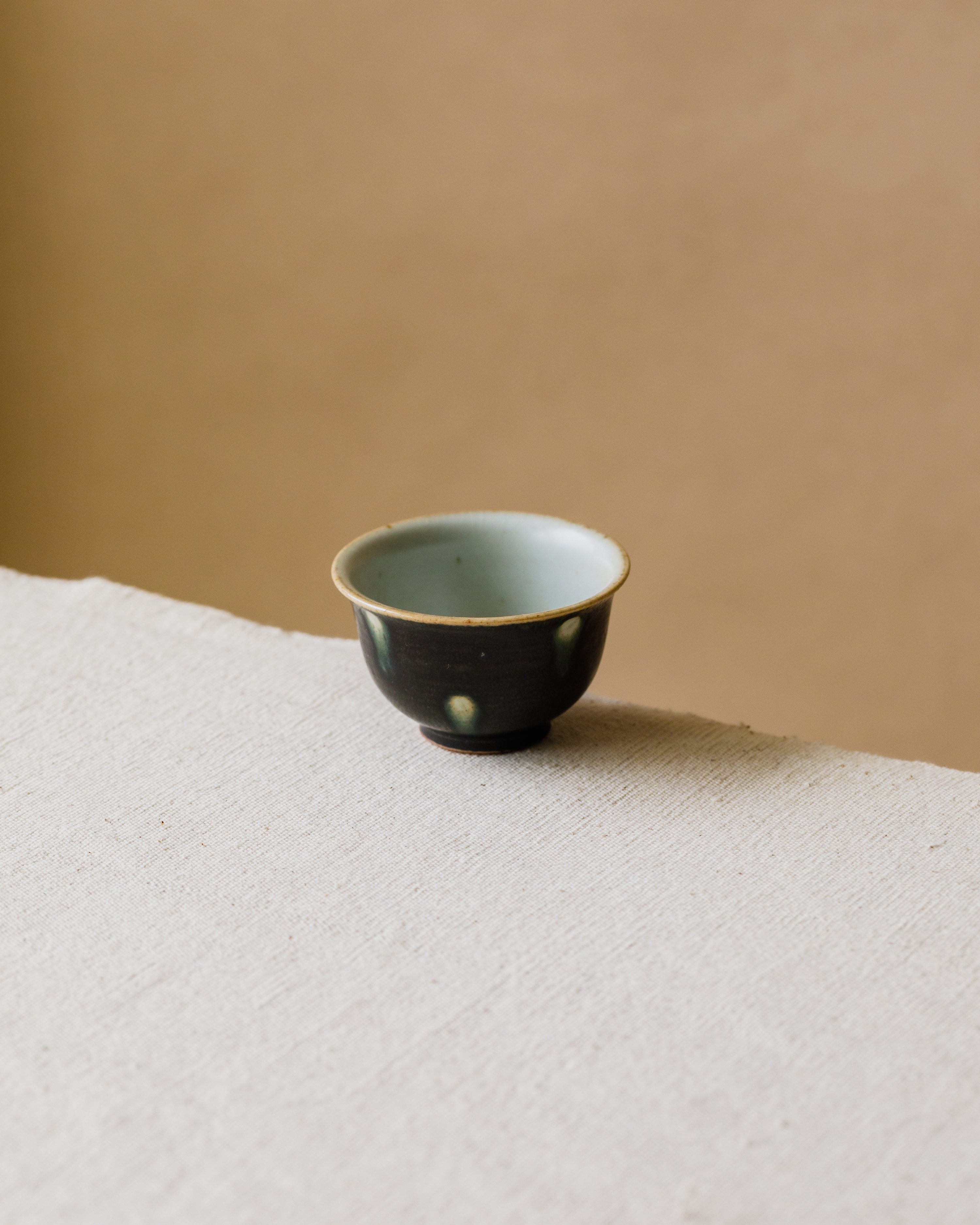 Cup Black Peacock in hand, peacock-iris pattern on matte black, Wang Xinghua gongfu teaware