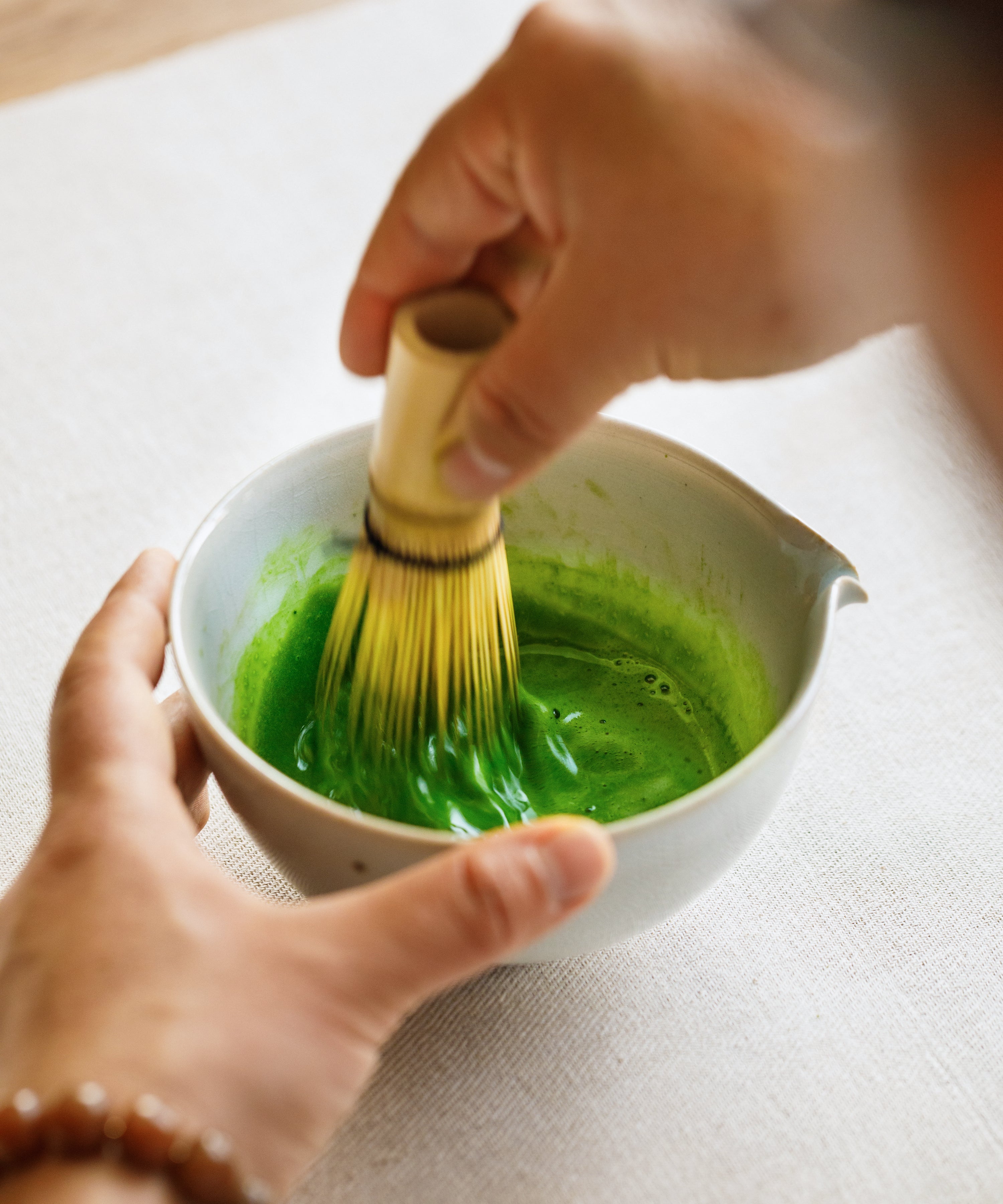 Whisking Kirari matcha with a bamboo chasen in a white ceramic bowl