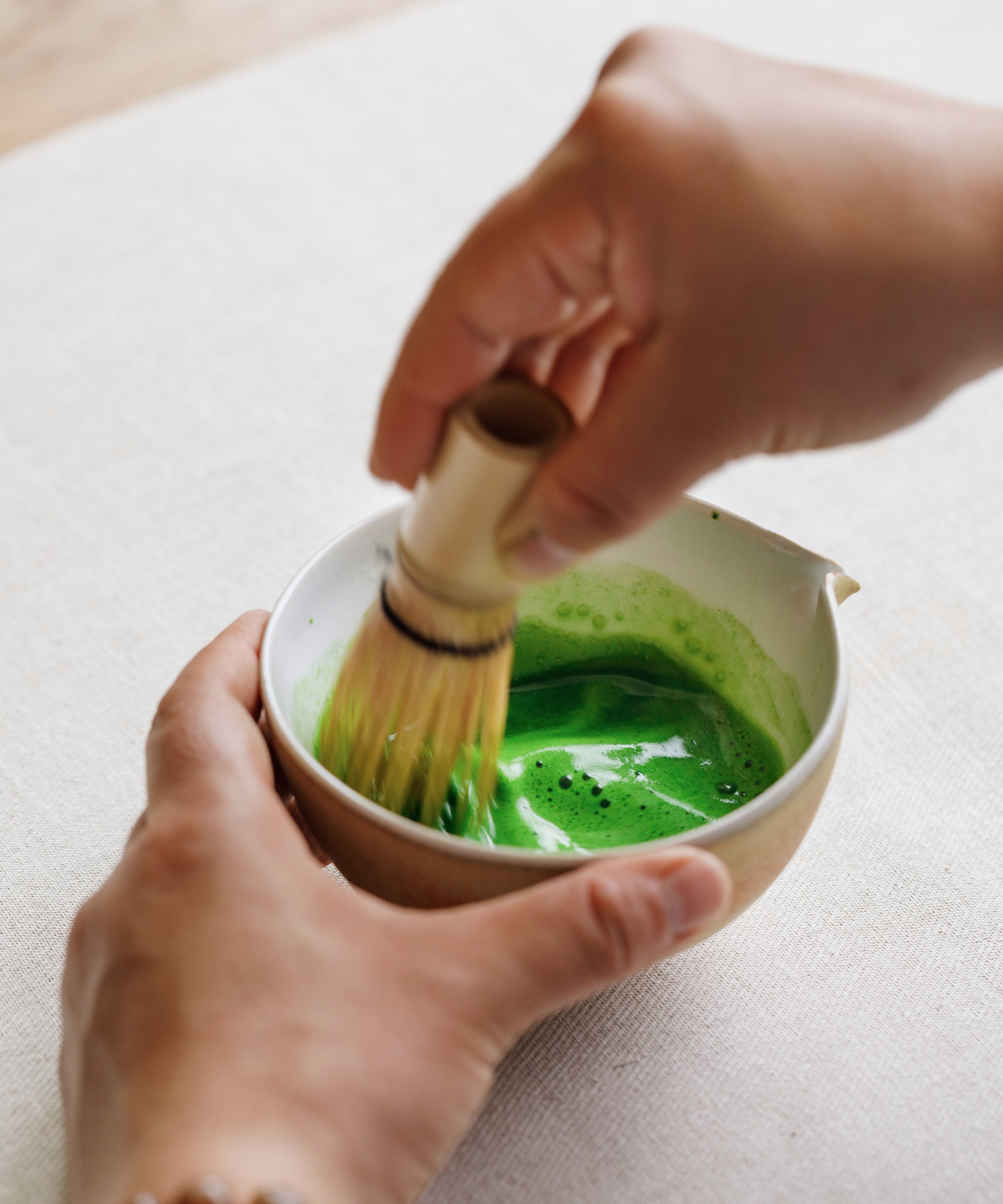 Whisking Oku Yutaka matcha with a bamboo chasen in a white ceramic bowl