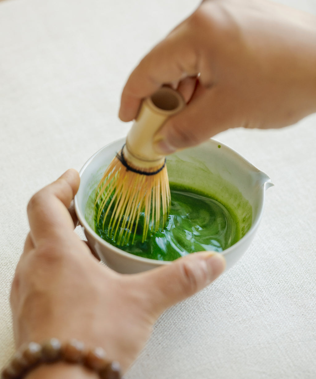 Hand scooping Saemidori matcha powder into a white preparation bowl