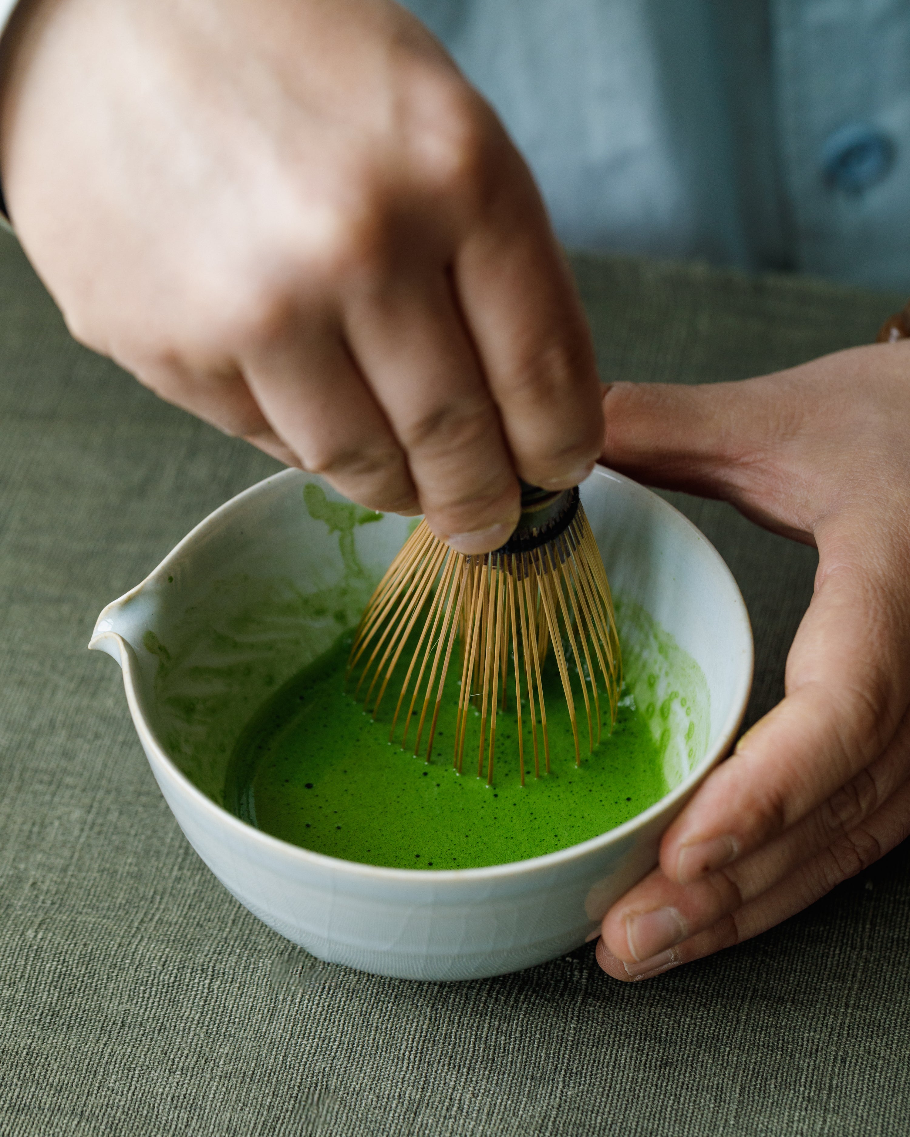 Hand whisking Matcha Hikari Japanese matcha with bamboo chasen in white bowl