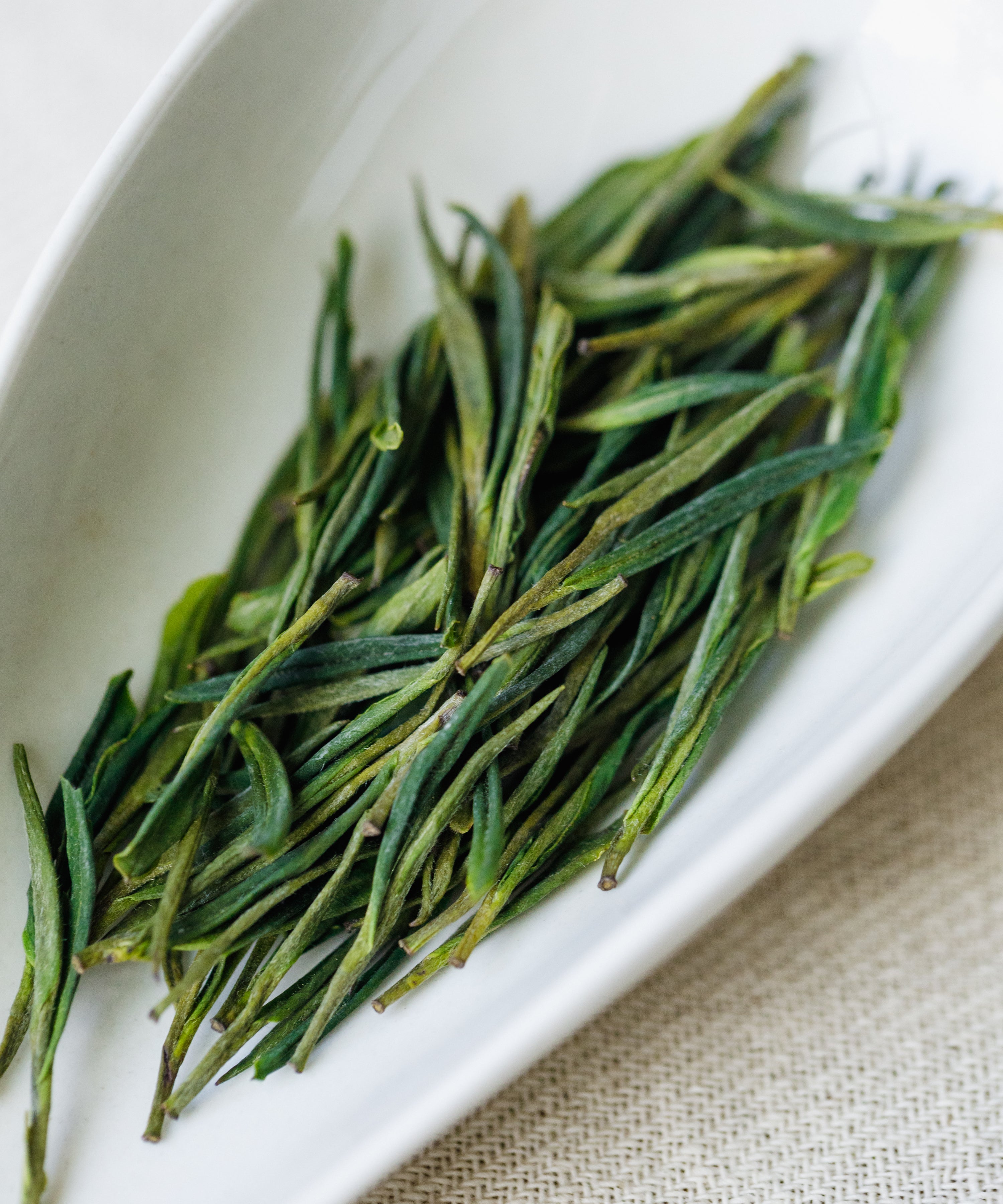 Dry Anji Baicha leaves on a white plate showing the slender white-leaf varietal
