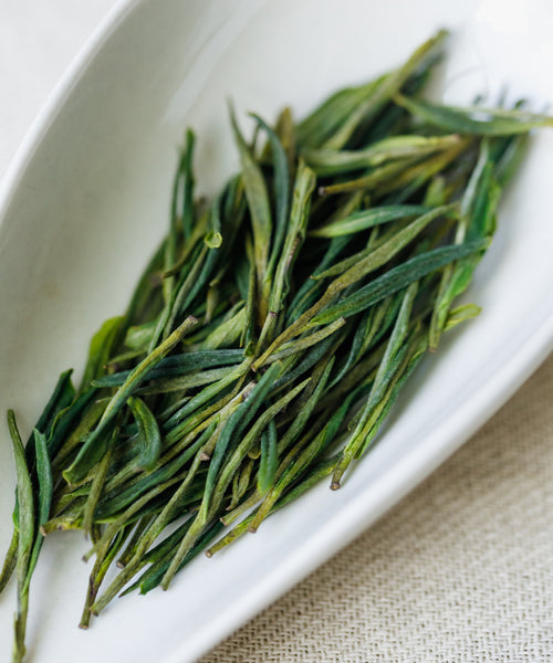 Dry Anji Baicha leaves on a white plate showing the slender white-leaf varietal