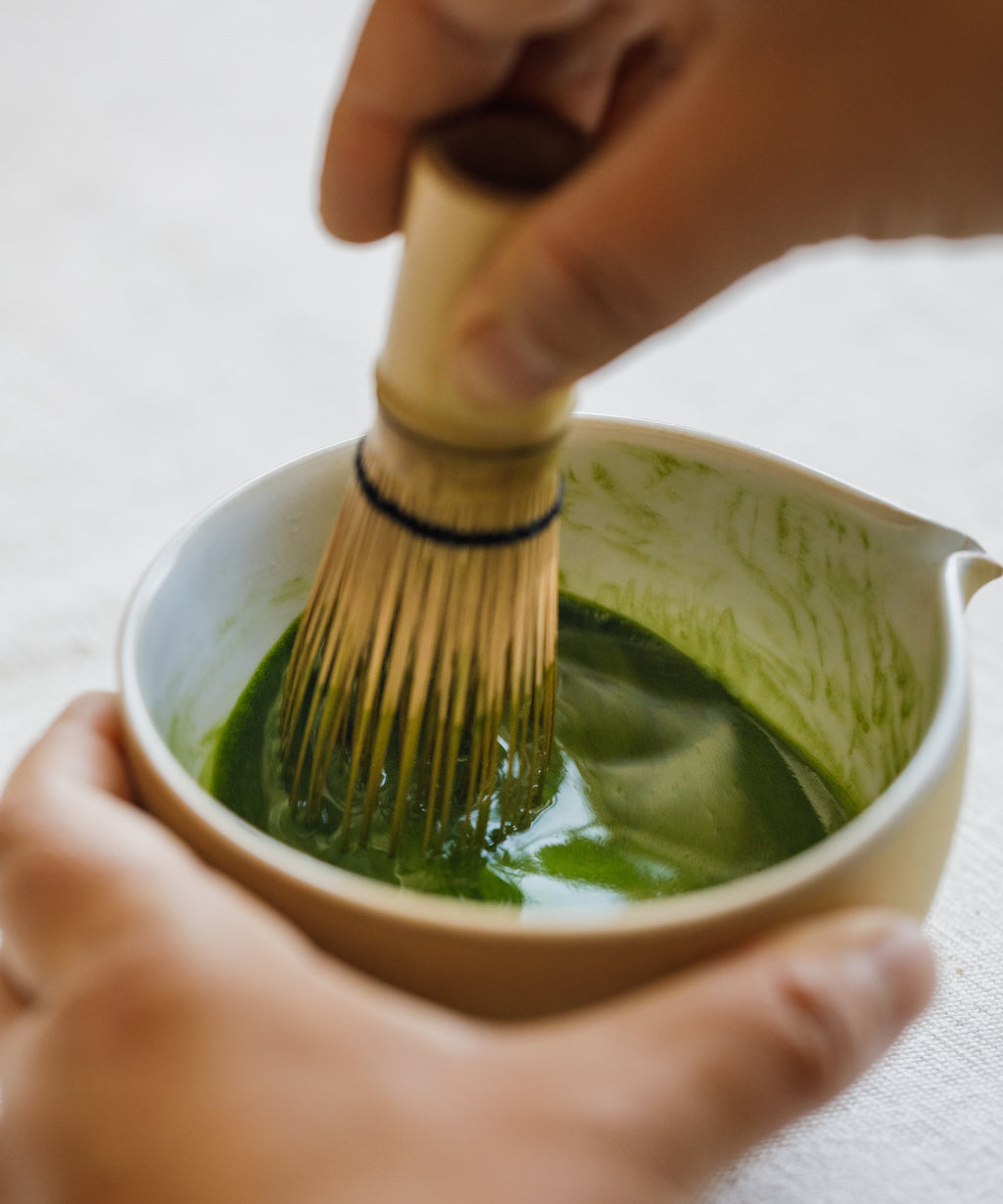 Whisking Tsuyu Hikari matcha with a bamboo chasen in a white ceramic bowl