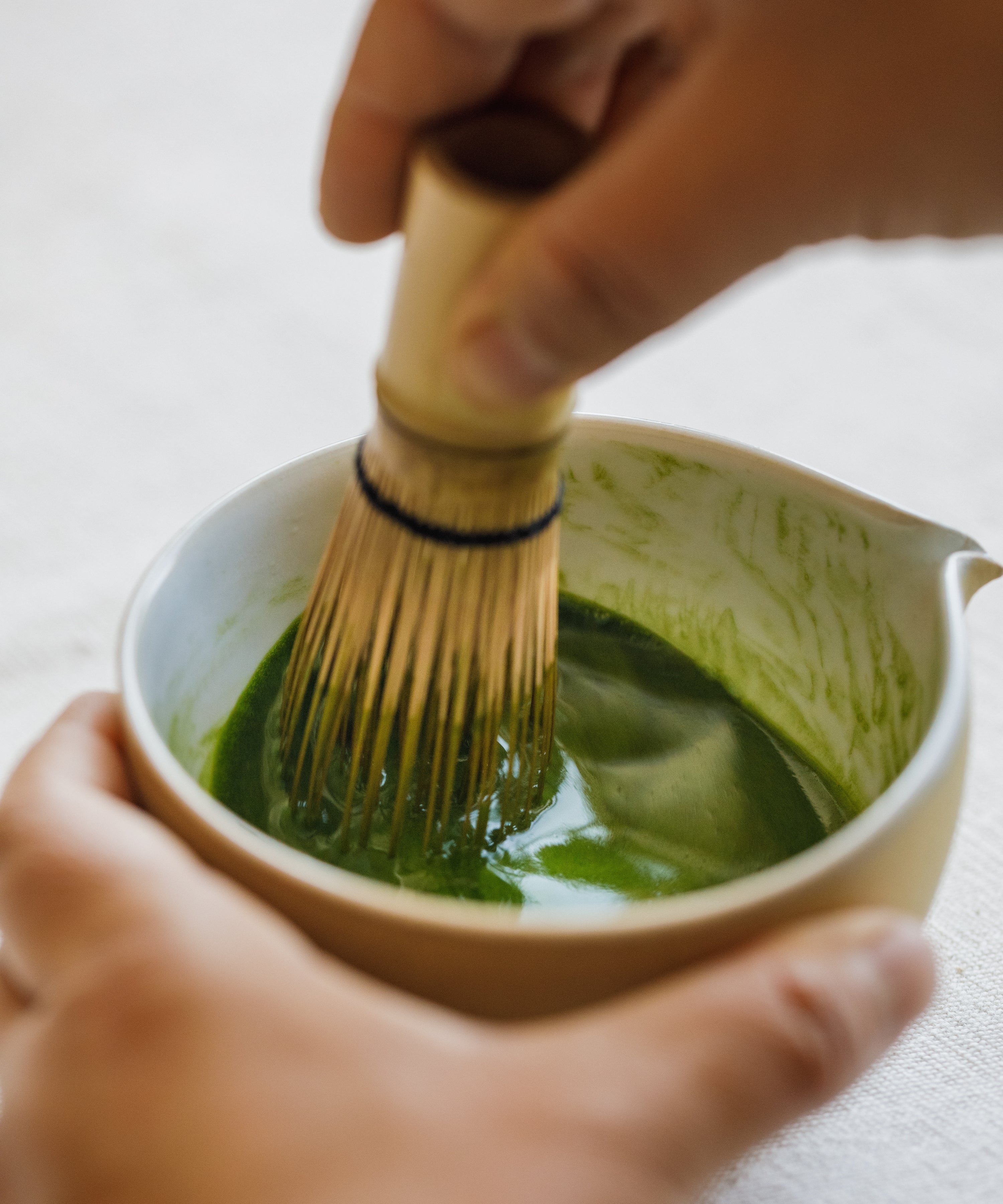Whisking Tsuyu Hikari matcha with a bamboo chasen in a white ceramic bowl