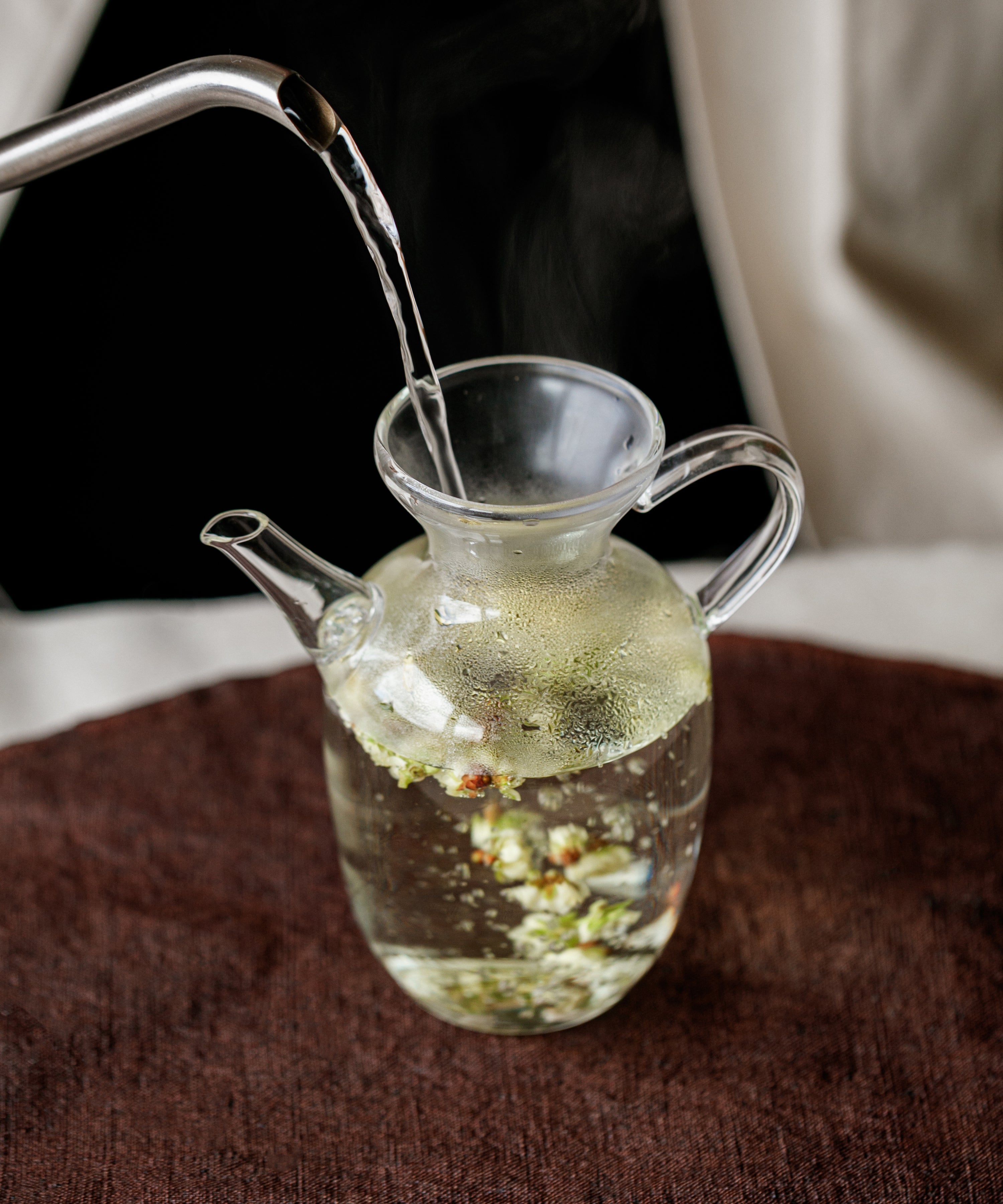 Hot water being poured over plum blossoms in a glass pitcher