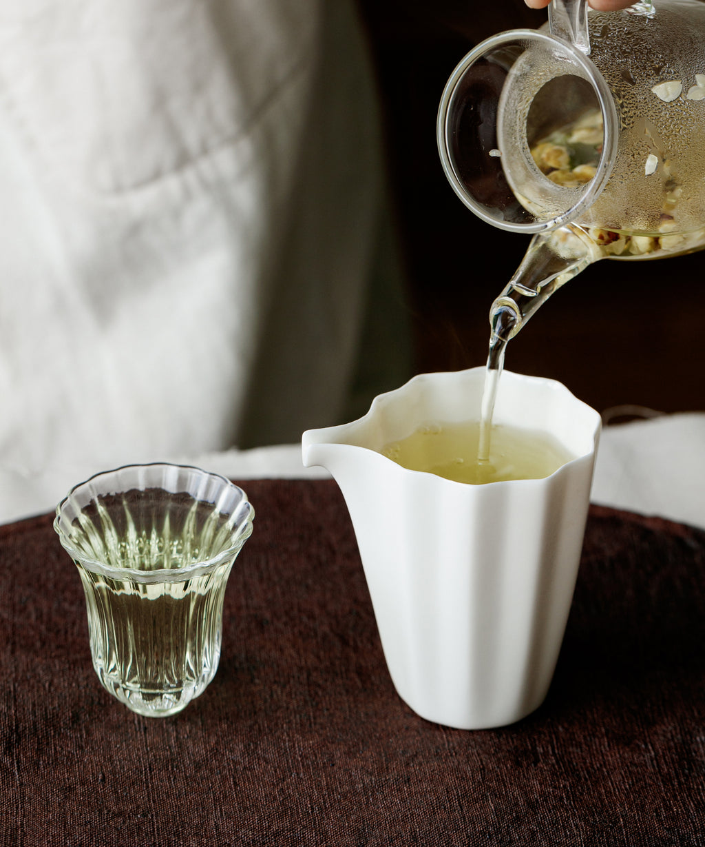 Brewed plum blossom infusion poured from a white gaiwan into a small glass cup