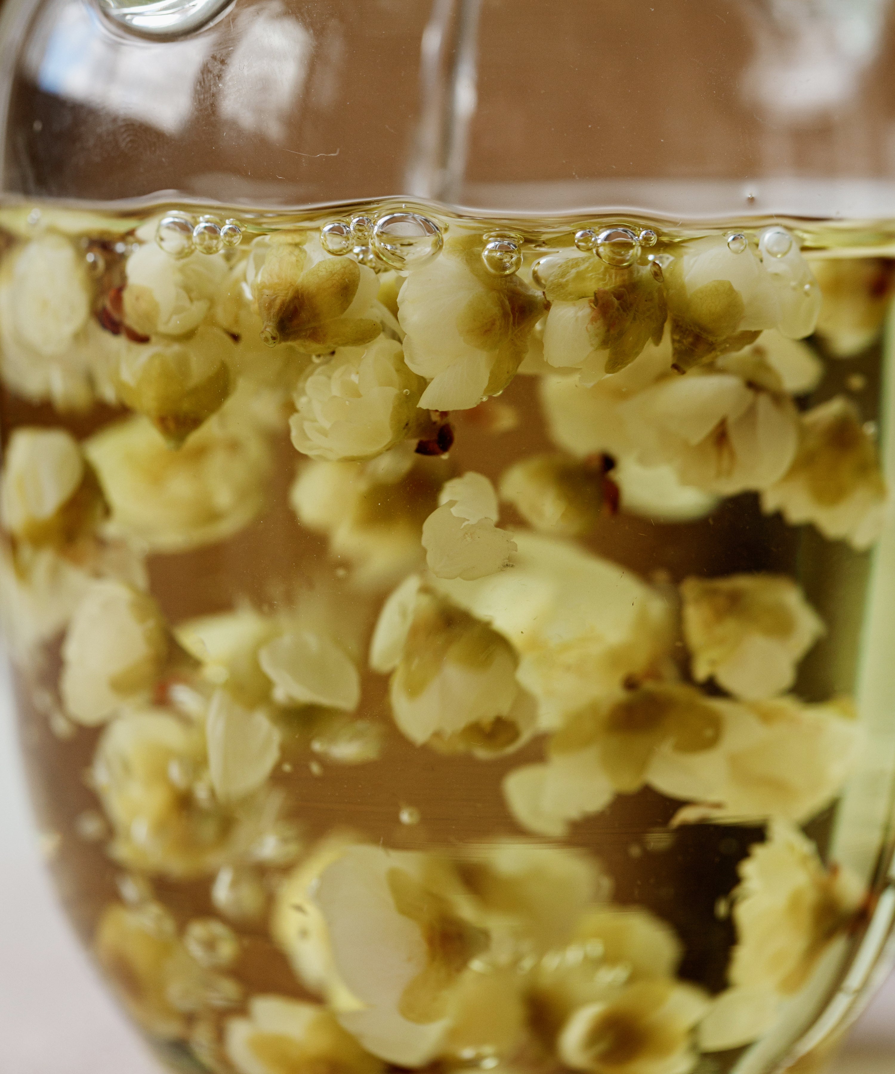 Plum blossom tisane in a glass pitcher, blossoms suspended in pale liquor